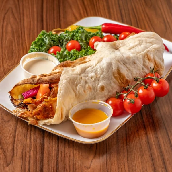 A chicken shawarma wrap with vegetables, two sauces, and cherry tomatoes on a white plate.