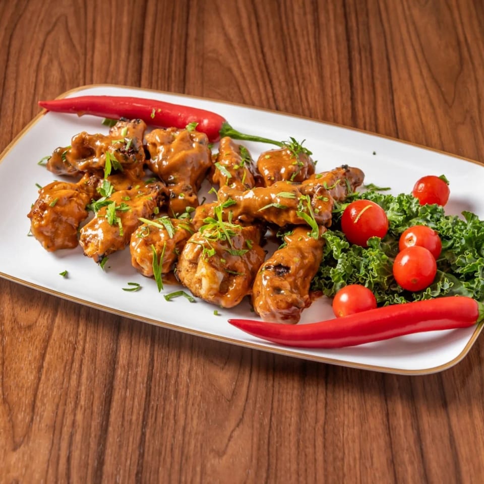 Chicken wings coated in a rich brown sauce, garnished with fresh herbs, red chilies, and cherry tomatoes.