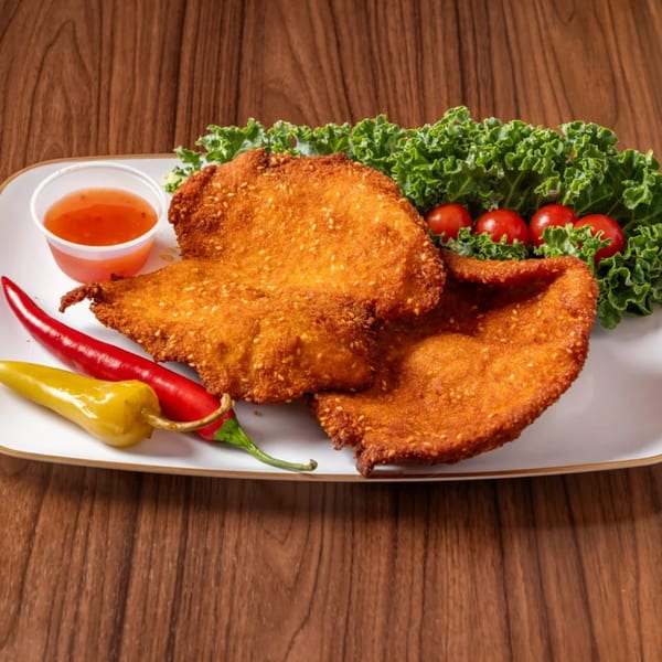 Two golden-brown fried chicken cutlets with sesame seeds, sweet chili sauce, peppers, kale, and cherry tomatoes.
