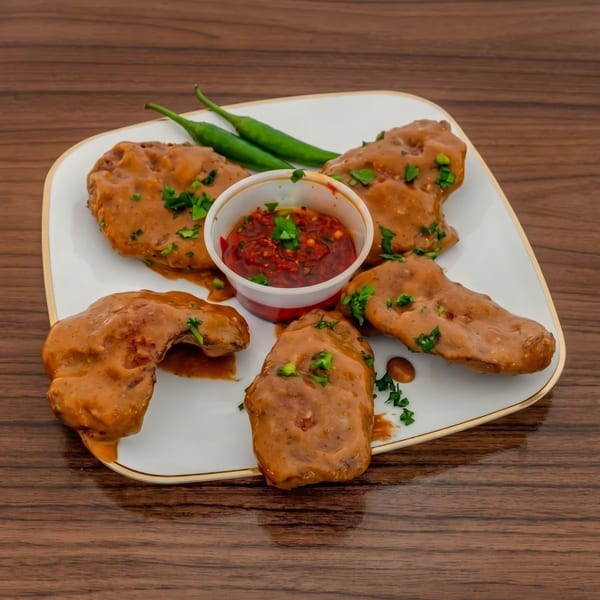 Five chicken wings covered in a creamy brown sauce with a side of red chili dip and green peppers.