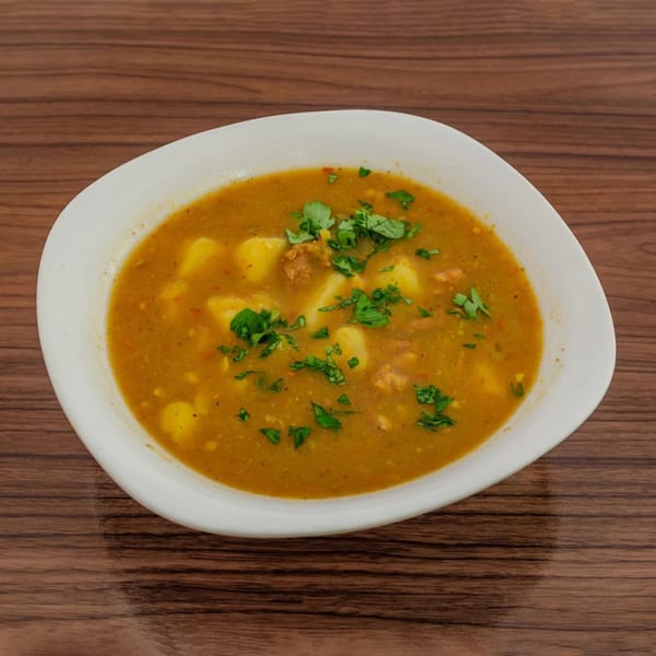 Hearty potato and meat stew with fresh cilantro in a white bowl on a wooden table.