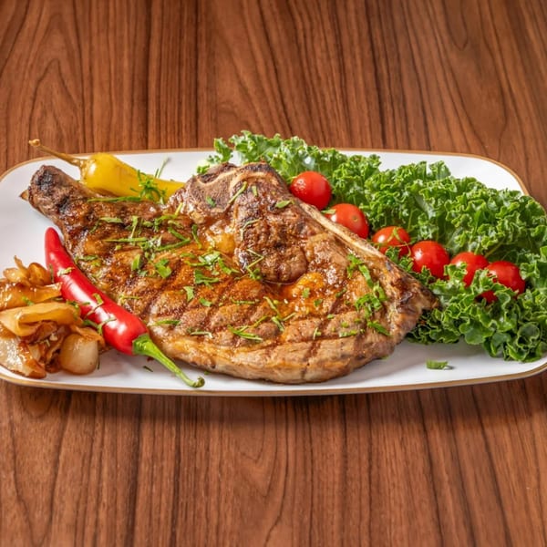 Grilled steak with peppers, onions, cherry tomatoes, and kale on a white plate.